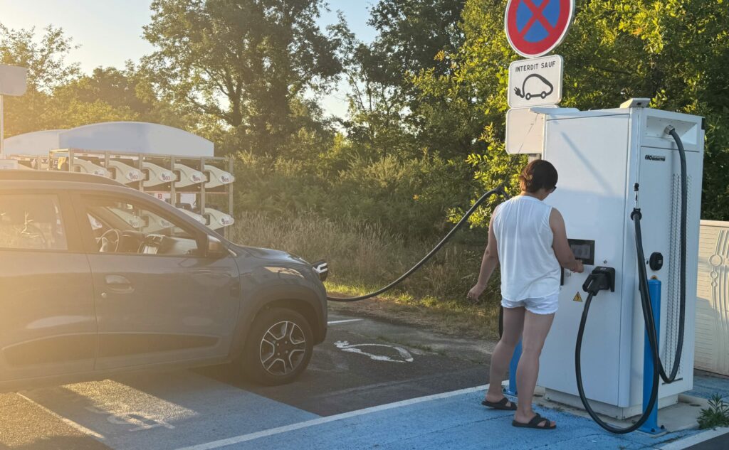 Woman using a charging point to recharge her electric car, illustrating intelligent technologies and lifestyle comfort.