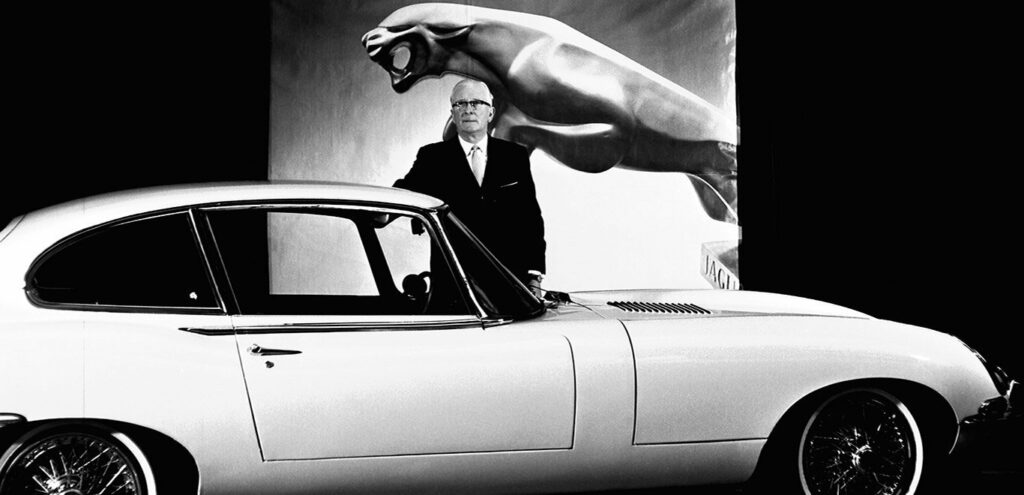 William Lyons founder of Jaguar with the Jaguar logo in the background