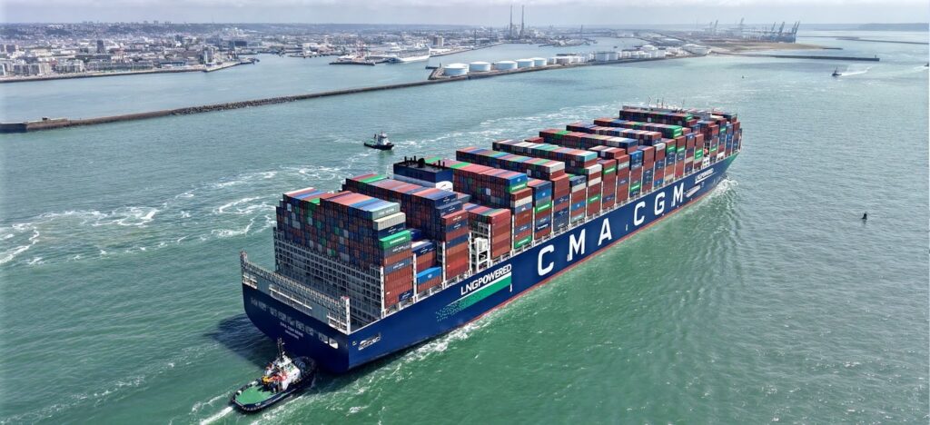 Aerial view of a large CMA CGM container ship sailing close to a port.